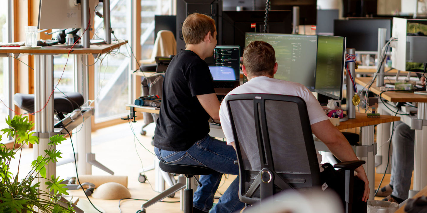 Mehrere MitarbeiterInnen von Vivid Planet die mit Freude an Ihren Computern sitzen uns arbeiten, eine Person trägt Lederhose